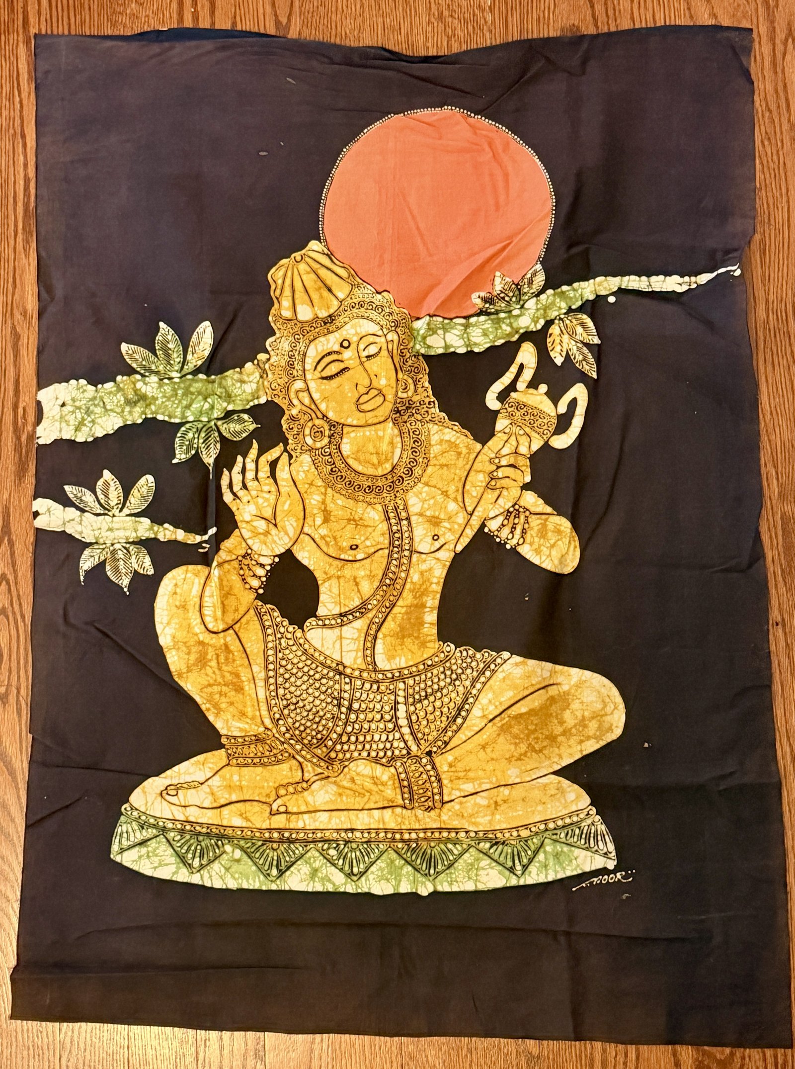 Batik signe NOOR, divinite doree assise sous un disque solaire orange, fond brun